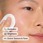 Close-up of a person applying The Ordinary's Milky Toner with a cotton pad. Text overlays highlight the product's benefits: Hydrates, Brightens, and Evens Texture & Tone for healthier-looking skin.